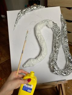 a person holding a paintbrush next to a piece of tin foil on a canvas