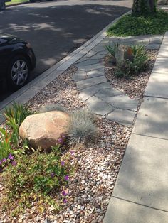 a car is parked on the side of the road next to a rock and plants