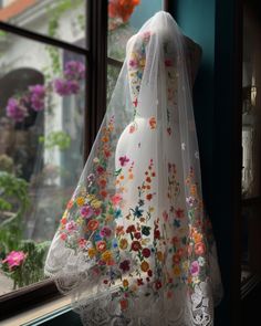 a wedding dress hanging on a window sill in front of a flowered wall