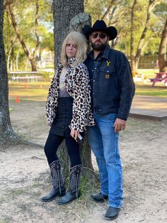 a man and woman standing next to each other in front of a tree wearing cowboy boots