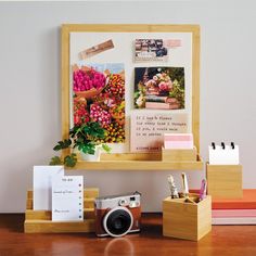 a wooden desk topped with a camera and lots of flowers next to a framed photograph