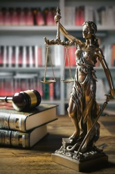 a statue of lady justice holding the scales of justice in front of books on a table - stock photo - images