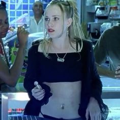 a woman with no shirt on standing in front of a counter and two other people behind her