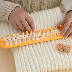 a person is holding a yellow and white comb on a knitted blanket with a teddy bear