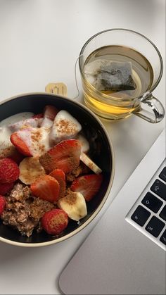 a bowl of cereal and strawberries next to a cup of tea