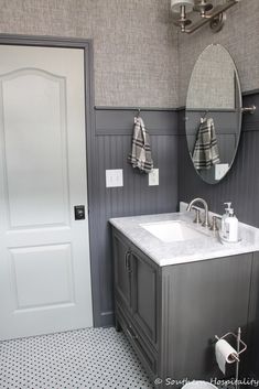 a white sink sitting under a bathroom mirror next to a door and toilet paper dispenser