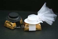 two black and white hats are sitting on top of gold foil wrapped boxes, one is wearing a tulle