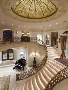 a grand piano is in the center of this large room with stairs and chandelier