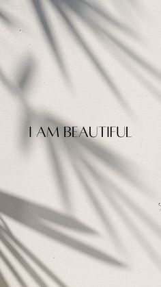 the word i am beautiful is written in black on a white wall with shadow from a palm tree