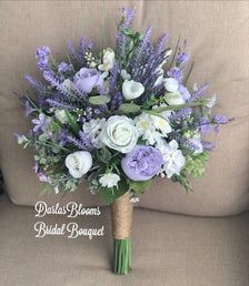 a bridal bouquet with lavenders, white roses and greenery on a couch