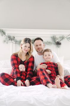 a man and woman are sitting on a bed with their two children in matching pajamas