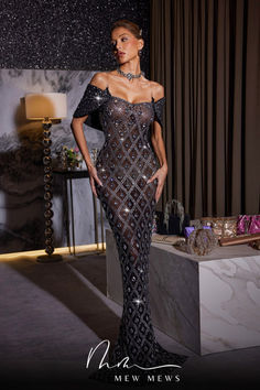 a woman in a black and silver gown standing next to a table with jewelry on it