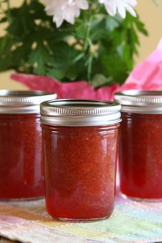 three jars filled with red liquid sitting on top of a table next to a pink flower