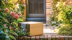 a box sitting on the ground in front of some bushes and flowers, near a door