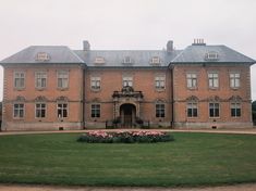 a large brick building sitting on top of a lush green field next to a flower garden