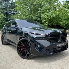 the front end of a black suv parked in a parking lot with trees behind it