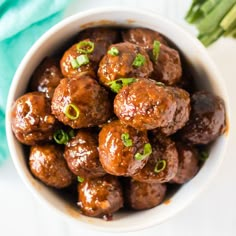 a white bowl filled with meatballs and green onions