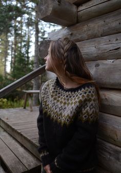 a woman sitting on a wooden bench next to a log cabin and looking up at the sky