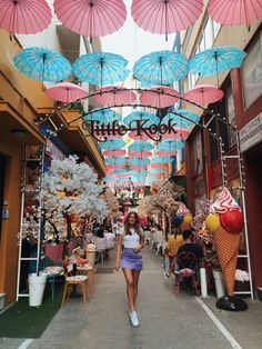 a woman is walking down the street in front of an ice cream shop with pink and blue umbrellas