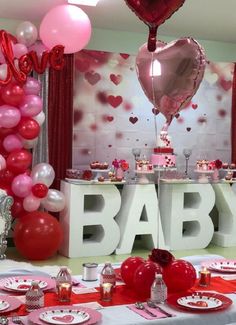 a baby shower is set up with pink and red balloons, plates, cups, and silverware