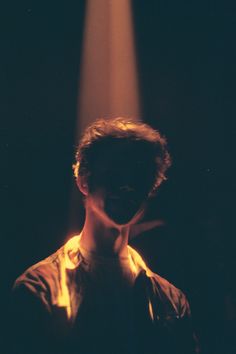 a man standing in front of a spotlight with his hands on his face and the light coming from behind him