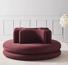 a large round couch sitting on top of a white floor next to a vase filled with flowers