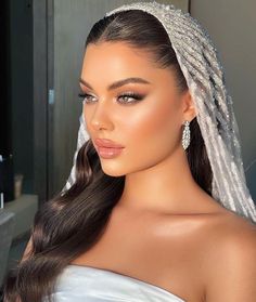 a woman wearing a bridal veil and diamond earrings with her hair in a ponytail