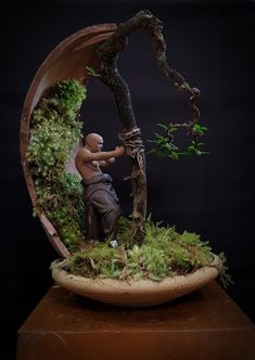 a man sitting on top of a wooden table next to a green plant covered in moss