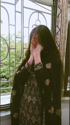 a woman standing in front of a window covering her face