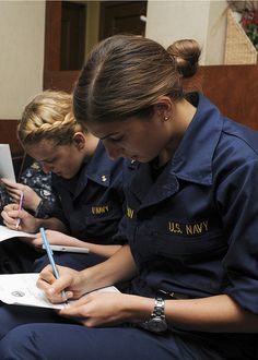 two women in navy uniforms sitting down writing on notebooks and taking notes from each other