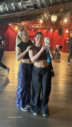 two women standing next to each other in a dance studio holding up their cell phones