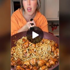 a woman in an orange shirt is holding a frying pan filled with spaghetti and chicken