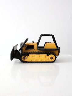 a yellow toy bulldozer sitting on top of a white table next to a black object