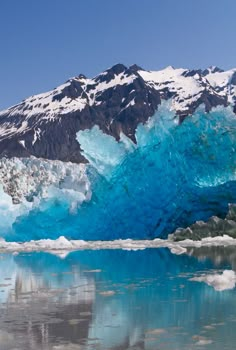 an iceberg with snow capped mountains in the background and water reflecting off it's surface