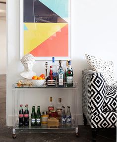 a bar cart with liquor bottles and drinks on it in front of a painting by the wall