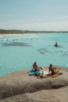 two people are sitting on the rocks near the water and one person is laying down