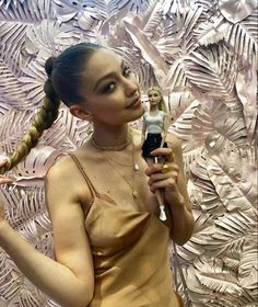 a woman holding a cell phone in her right hand and looking at the camera while wearing a gold dress