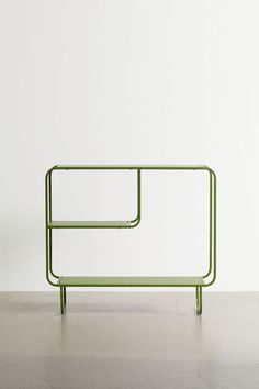 a green shelf sitting on top of a cement floor next to a white wall,