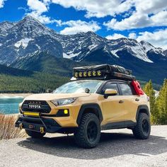 a yellow suv parked on the side of a mountain road with mountains in the background