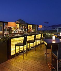 an outdoor bar is lit up at night with lights on the tables and stools