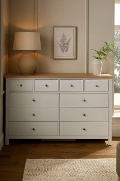 a white dresser sitting in front of a window with a lamp on top of it