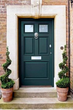 a green front door with two potted plants