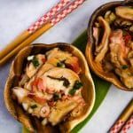 two small bowls filled with food sitting on top of a green leaf next to chopsticks