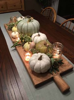 a wooden table topped with white pumpkins and greenery next to candles on top of a cutting board