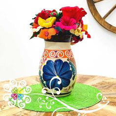 a colorful vase with flowers in it sitting on a table next to a green place mat