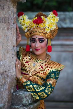 a woman dressed in an elaborate costume leaning against a stone wall with flowers on her head