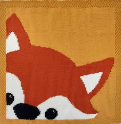 an orange knitted cushion with a red fox on it's face and black eyes