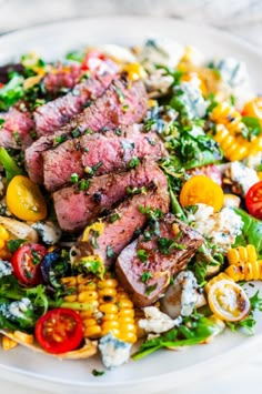 steak and corn salad on a white plate with tomatoes, onions, lettuce