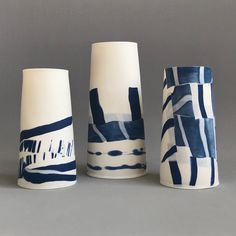 three ceramic vases sitting next to each other on a gray surface with white and blue designs