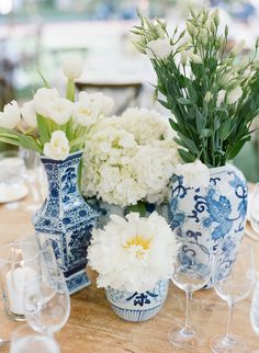 a table topped with blue and white vases filled with flowers next to wine glasses